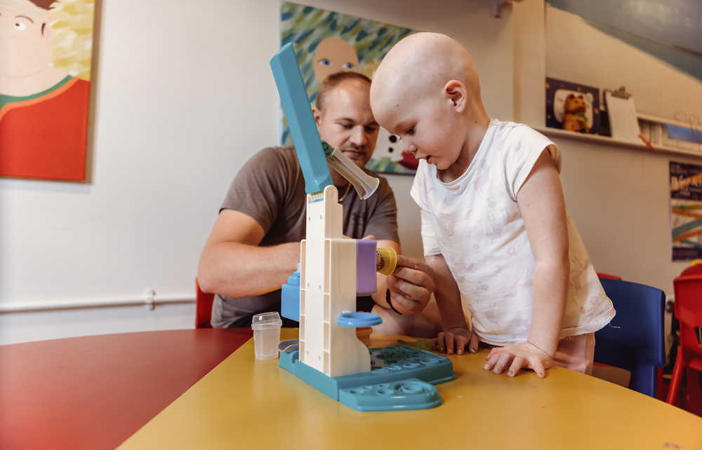 A little girl playing with toys on a table next to her dad