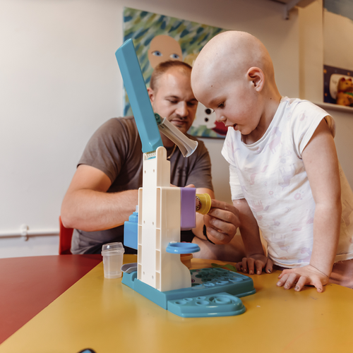 A little girl playing with toys on a table next to her dad