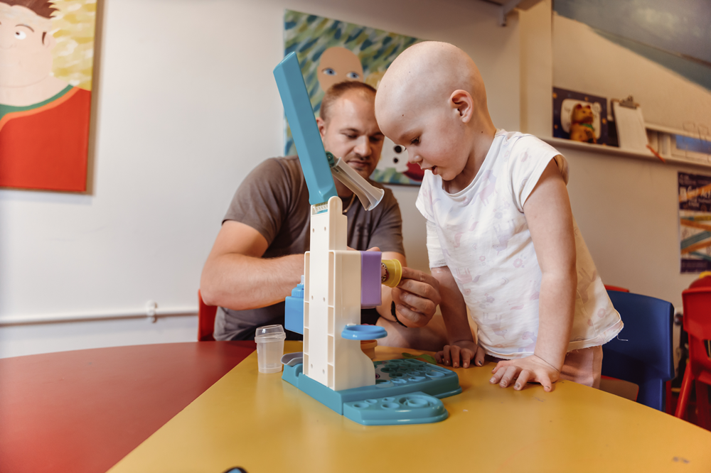 A little girl playing with toys on a table next to her dad