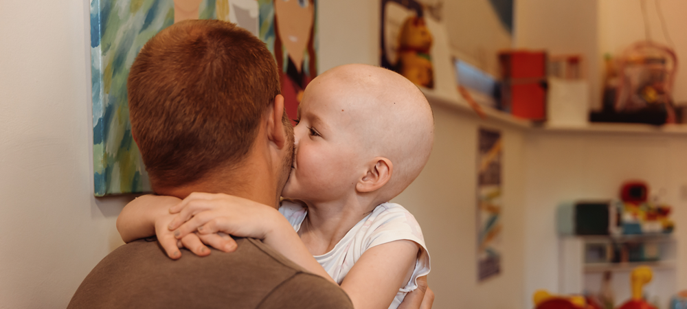 A little girl being held by her dad. She's kissing him on the cheek