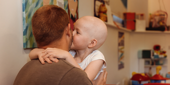 A little girl being held by her dad. She's kissing him on the cheek