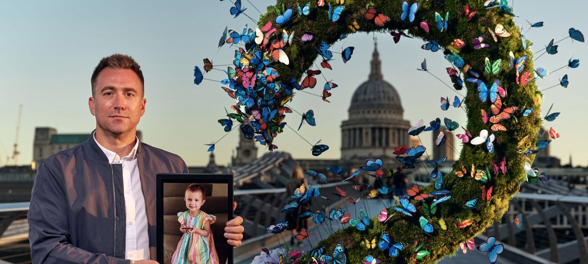 A GOSH parent holds a picture of his late daughter outside St Paul's Cathedral, surrounded by a colourful butterfly installation.