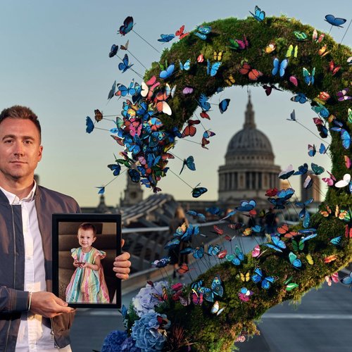 A GOSH parent holds a picture of his late daughter outside St Paul's Cathedral, surrounded by a colourful butterfly installation.