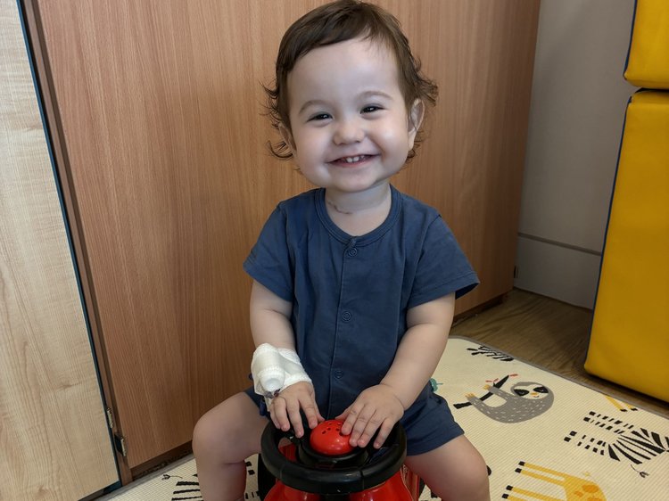 Casey smiles at the camera while sitting on a toy car