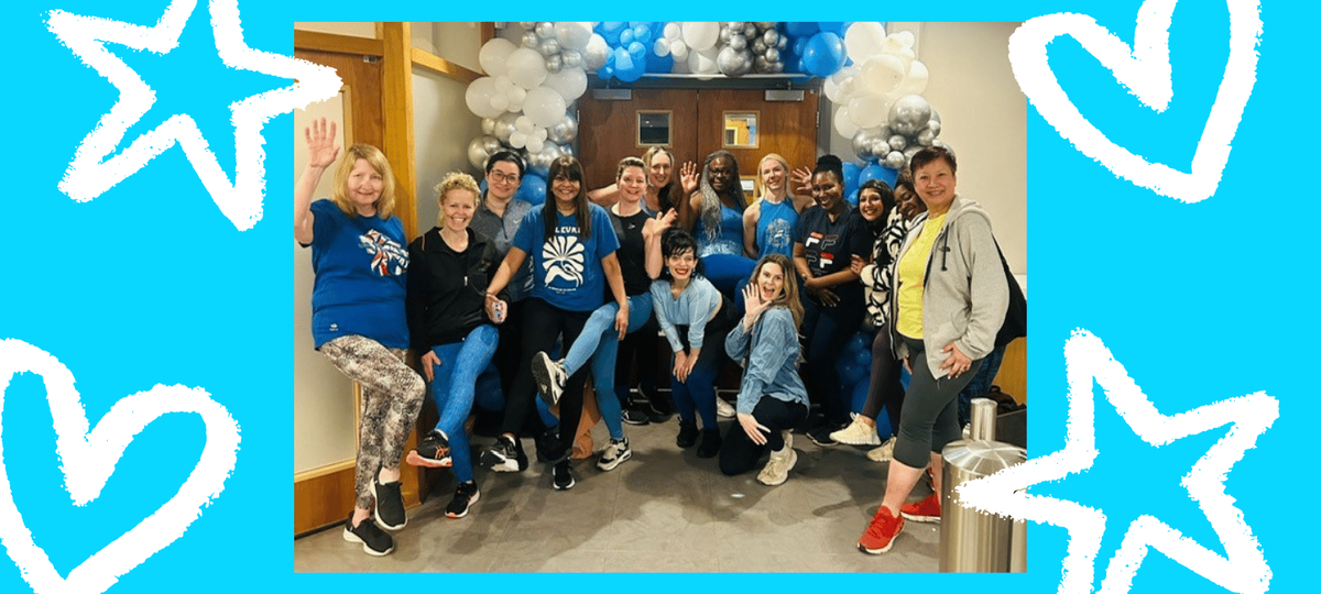 A group of 14 people posing and smiling in front of a balloon arch