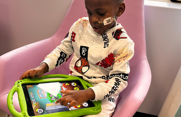 A little boy wearing Spiderman pyjamas playing on a tablet in hospital