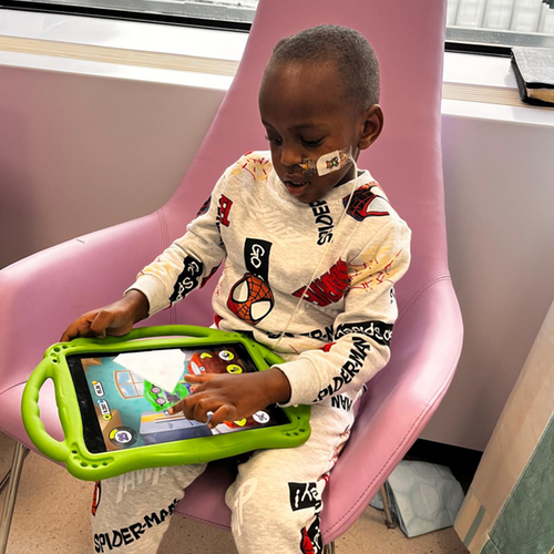 A little boy wearing Spiderman pyjamas playing on a tablet in hospital