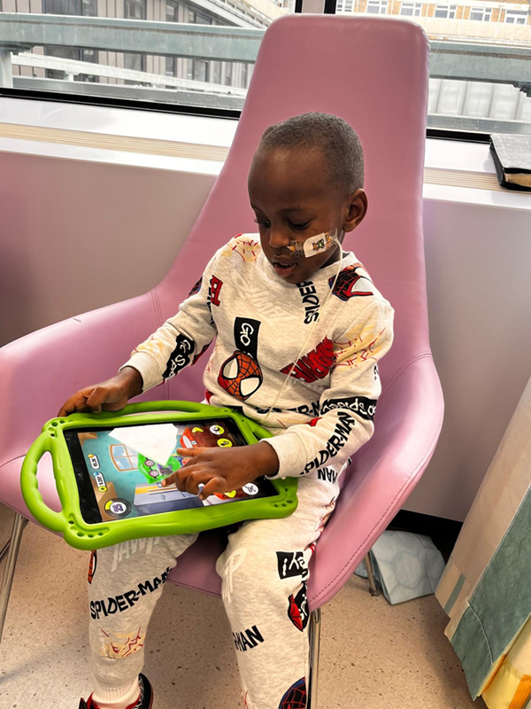 A little boy wearing Spiderman pyjamas playing on a tablet in hospital