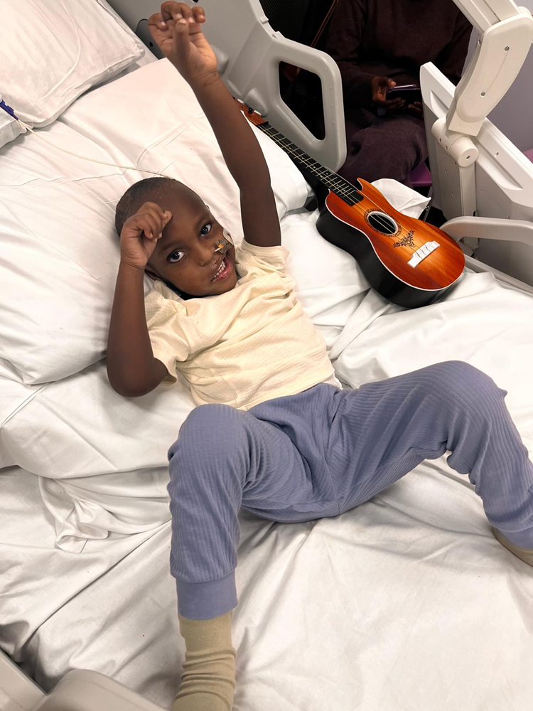 A little boy lying in a hospital bed next to a guitar