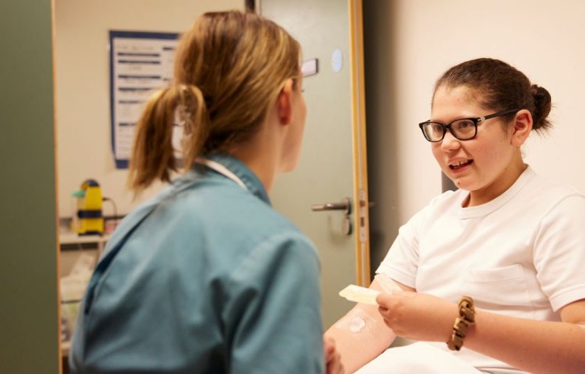 nurse sits with teenage girl in hospital room