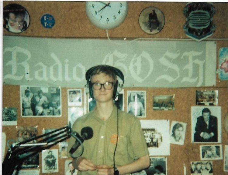 Vintage style photo of Paul presenting on 'Radio GOSH' after his valve replacement surgery when he was 17 years old. He can be seen in a studio, wearing headphones and standing in front of a mic. It says Radio GOSH in the background.