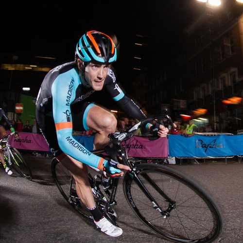 Professional cyclist on bike mid-race. People cheer him on.