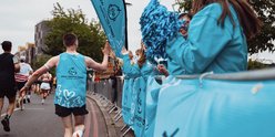 Image of a TeamGOSH runner wearing a blue GOSH Charity vest who is passing a GOSH cheer point along the route of their run.