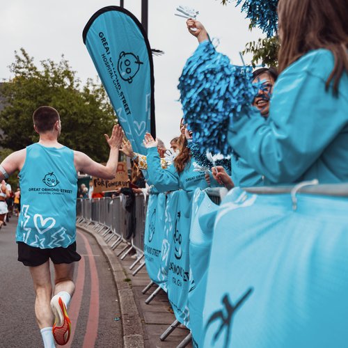 Image of a TeamGOSH runner wearing a blue GOSH Charity vest who is passing a GOSH cheer point along the route of their run.