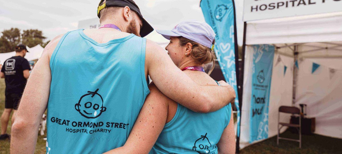Two Hackney Half runners have their arms around each other, wearing blue GOSH branded running vests. The photo is taken from behind so we can't see their faces.
