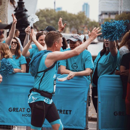 A man running the London Marathon run past a GOSH branded cheer point