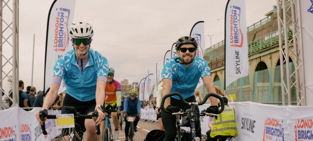 Two TeamGOSH Cyclists passing the finish line at the 2025 London to Brighton Cycle.