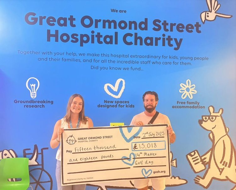 A man stands with a cheque outside a Great Ormond Street Hospital Charity sign.