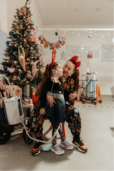 Girl on Berlin Heart machine with her mum in front of Christmas tree