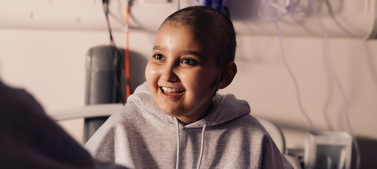 Teenage girl sits in hospital bed, smiling at person opposite her
