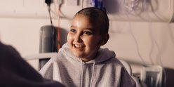 Teenage girl sits in hospital bed, smiling at person opposite her