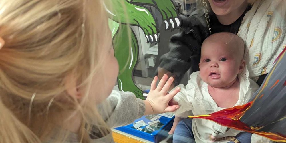 Baby girl looking through window at her sister while in hospital.
