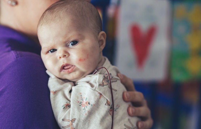 Baby in hospital room. She is looking to camera.