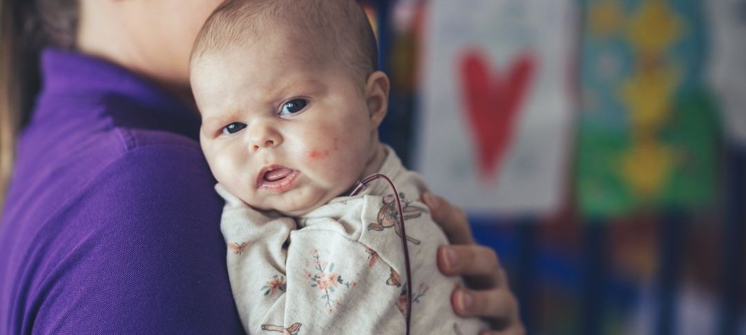 Baby in hospital room. She is looking to camera.
