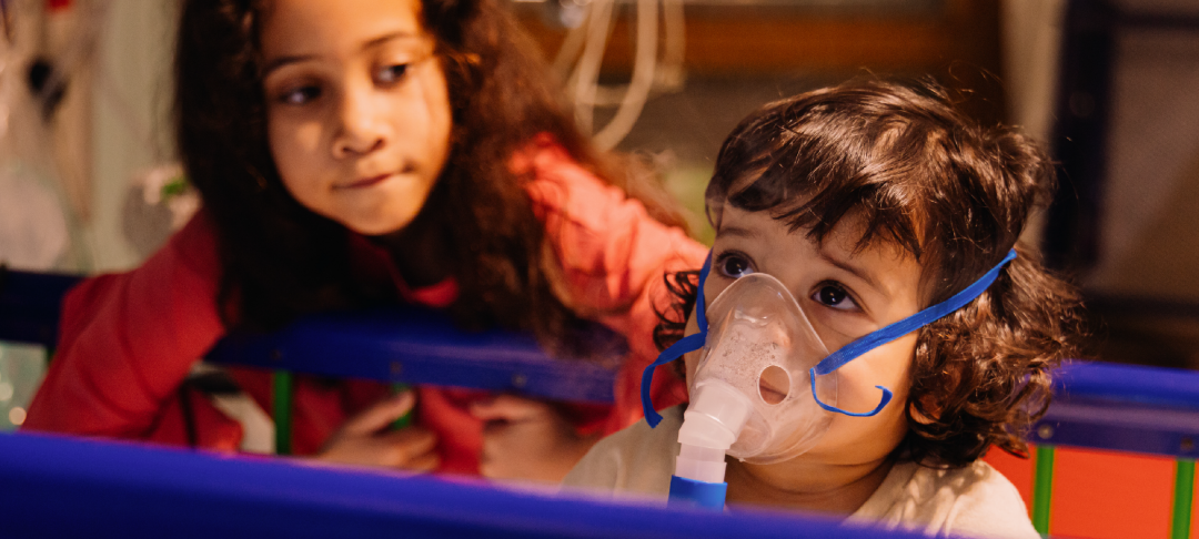 Reggie, 21 months, at GOSH wearing a mask to help him breathe while his sister Nyla, 7, watches on
