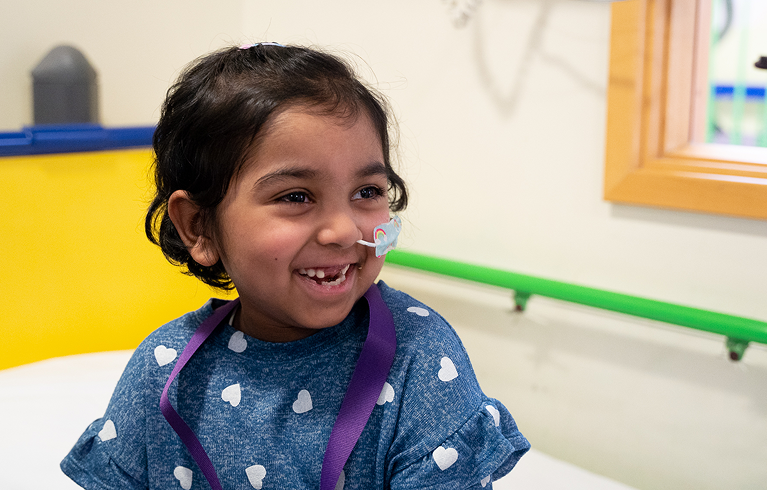 Little girl with feeding tube sitting on bed and smiling