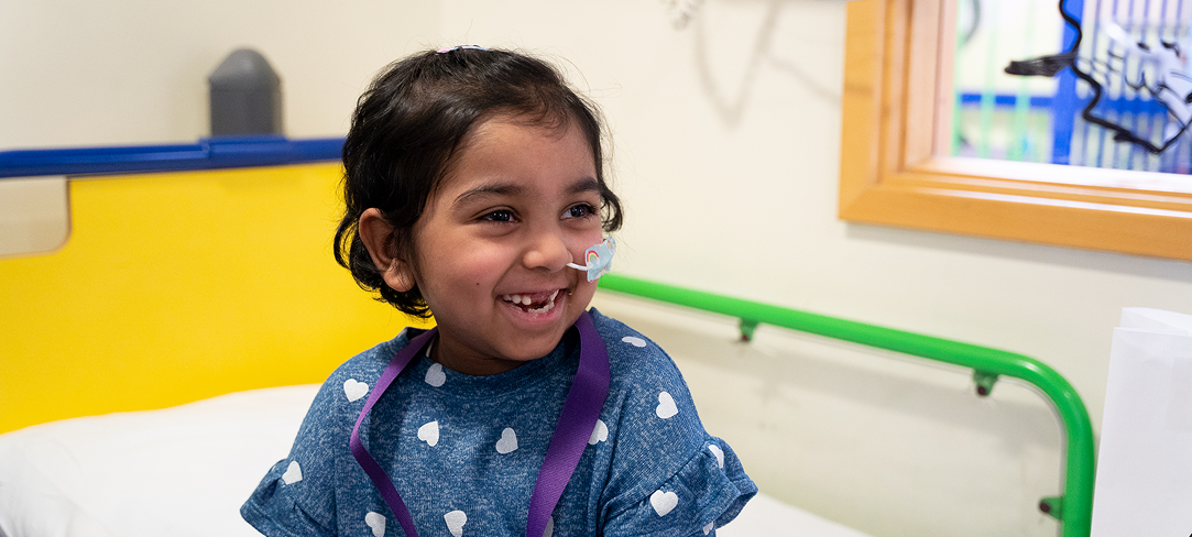 Little girl with feeding tube sitting on bed and smiling