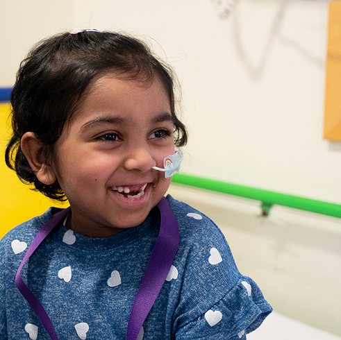 Little girl with feeding tube sitting on bed and smiling