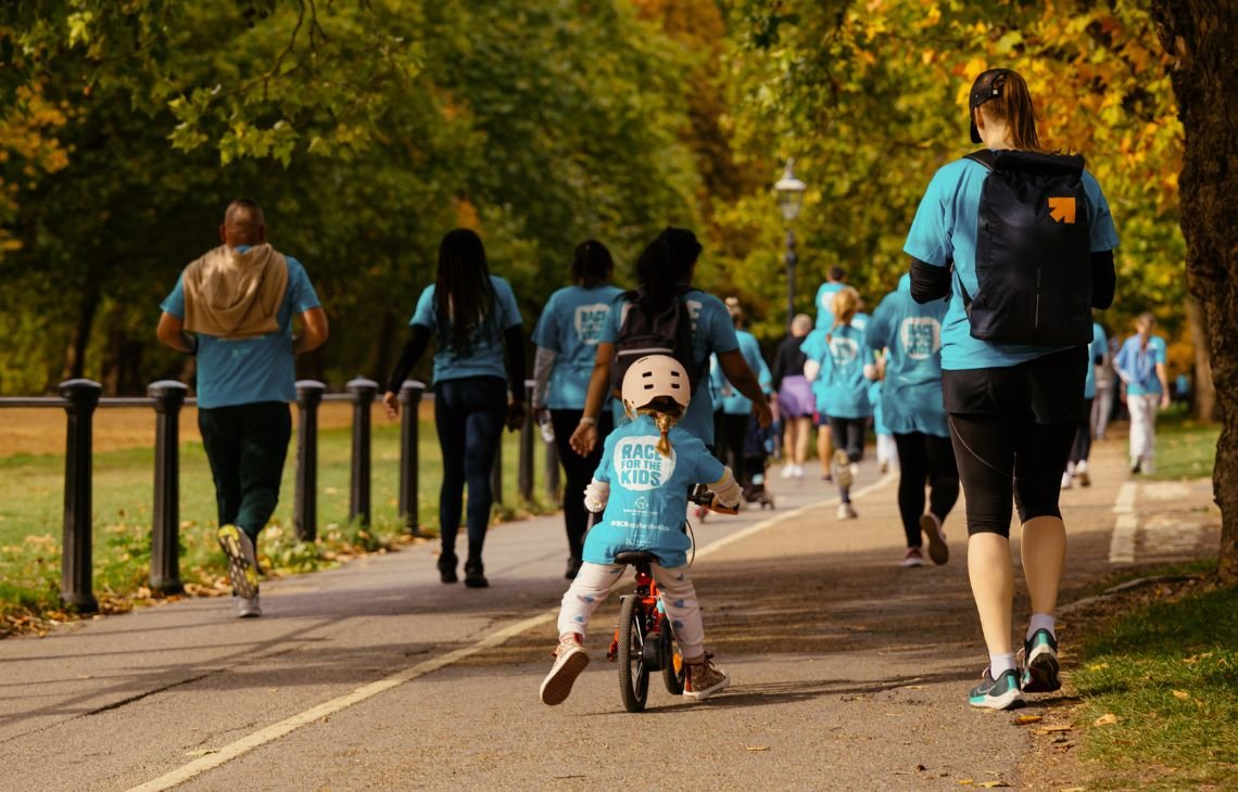 A young girl rides a bike through Hyde Park in autumn, sharing the path with joggers and walkers.