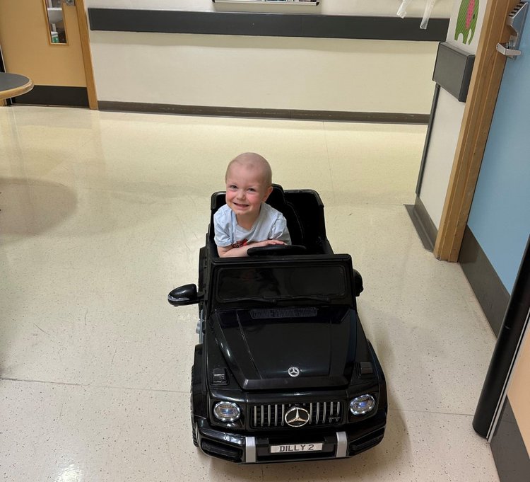 Hugo sitting in toy car in oncology ward. Smiling and looking to camera.