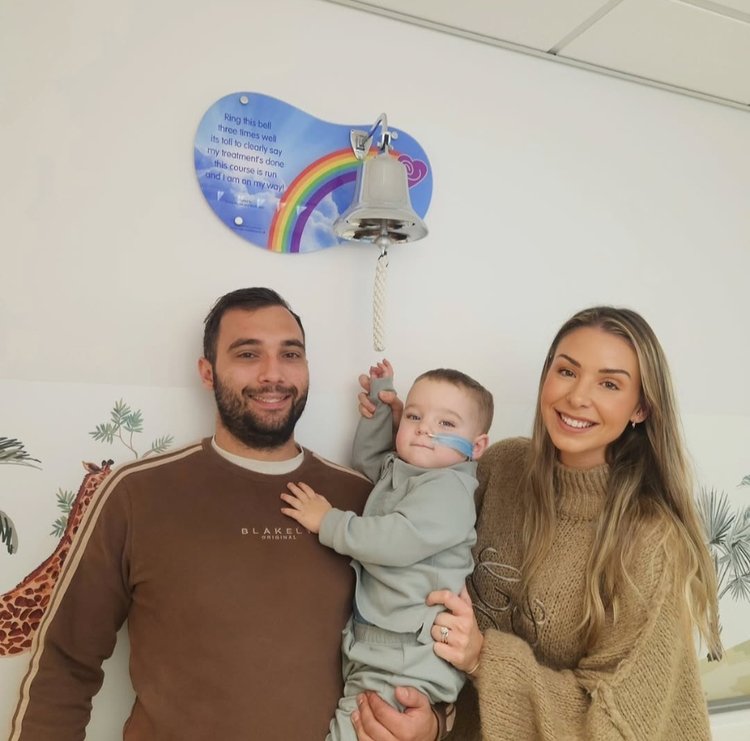 A little boy ringing the end of treatment bell with his parents