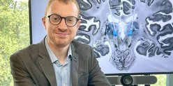 A researcher sat in front of a screen with a brain scan on it