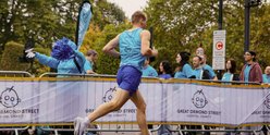 A runner wearing a blue GOSH Charity branded running vest runs past a white GOSH Charity banner