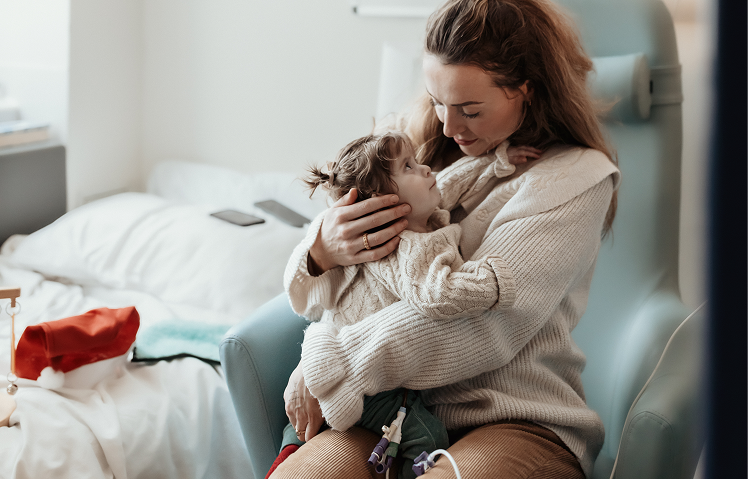 A little girl sits with her mum. A santa had can be seen next to them.