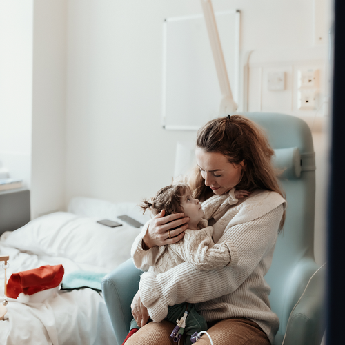 A little girl sits with her mum. A santa had can be seen next to them.