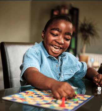 Little boy smiling and playing board game. He is sitting on a chair in his lounge at home.