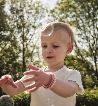 GOSH patient Jess in a sunny garden trying to catch bubbles