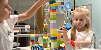 Siblings playing with building blocks on a hospital bed