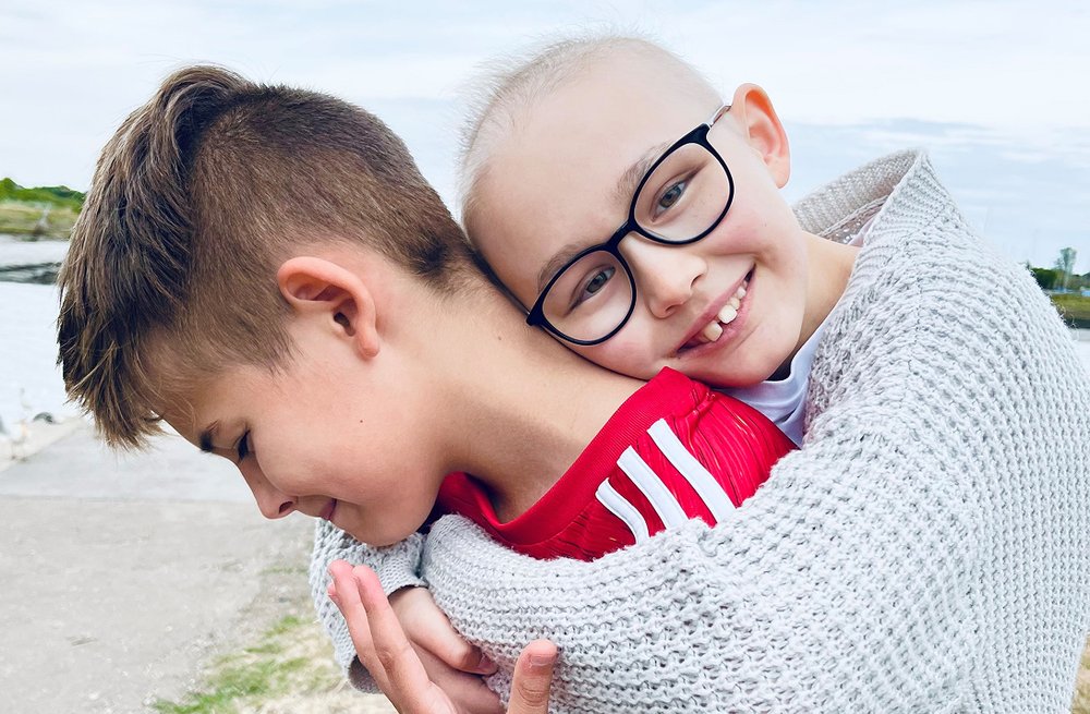 Teenage girl hugging boy outside on a path. Both smiling.
