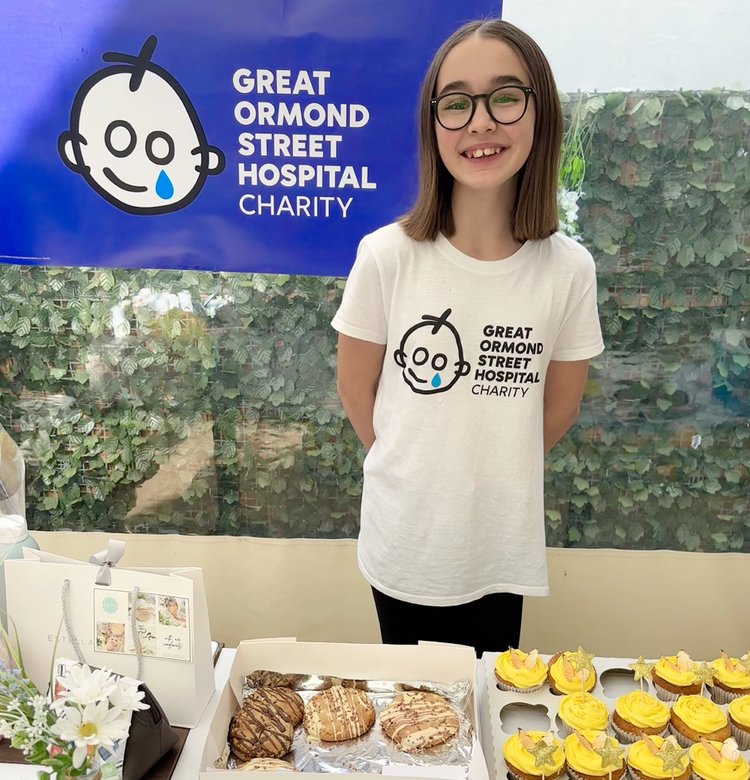Teenage girl hosting bake sale. GOSH Charity banner in background.