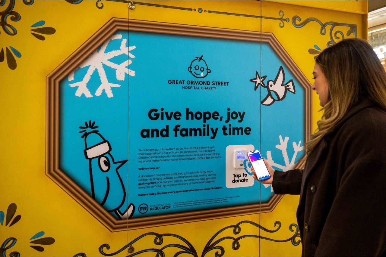A woman taps to donate on the St Pancras X GOSH Charity Christmas tree
