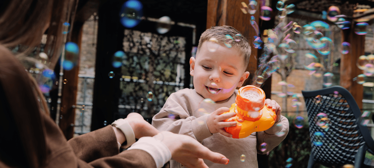 A young boy playing with bubbles coming out of an orange toy camera