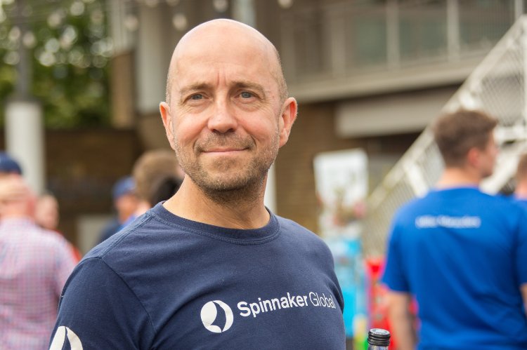 A man smiles to camera. He is standing outside, at an event.
