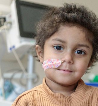 Photo of Yumna sitting on hospital bed, looking to camera