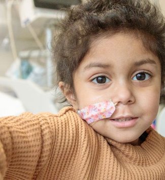 Photo of Yumna sitting on hospital bed, looking to camera and holding a toy wand