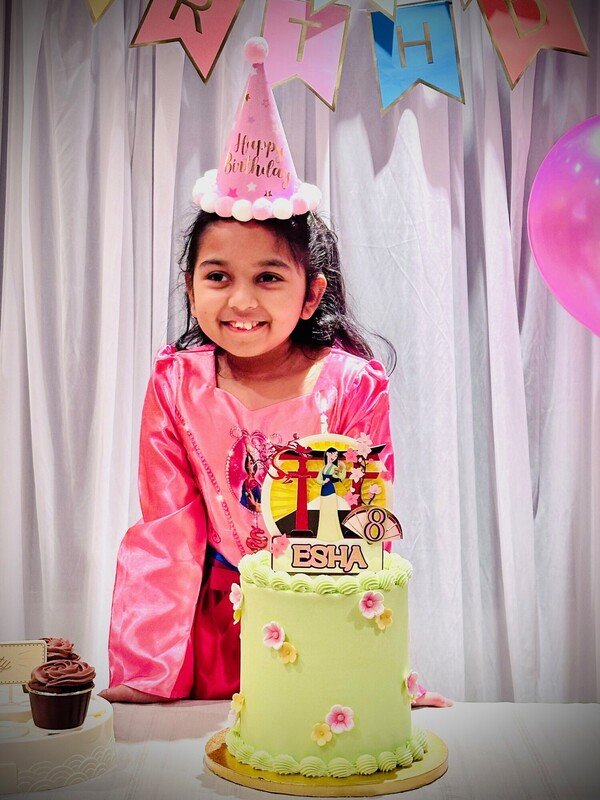 Young girl with a birthday hat on standing behind a two layered birthday cake